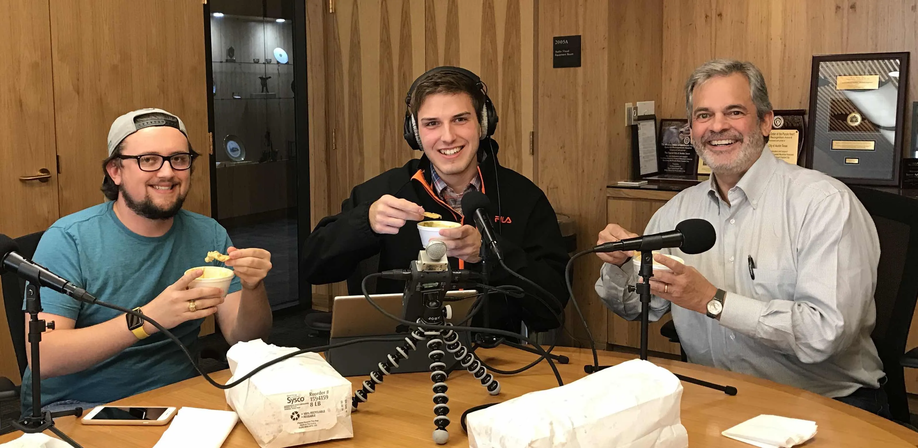 Daulton Venglar, Bryce Seifert, and Austin Mayor Steve Adler hold up queso and chips in front of podcasting equipment